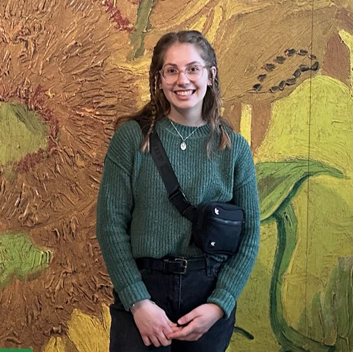 girl with brown hair in braids, 圆框眼镜, 绿色的毛衣, in front of van gogh's sunflowers painting